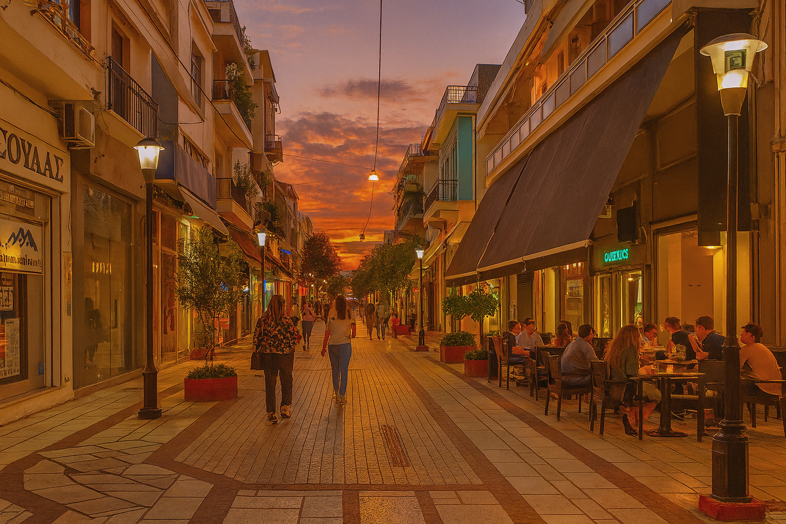 Abendstimmung in der Fußgängerzone von Arta mit beleuchtetem Straßencafé und Spaziergängern unter einem malerischen Sonnenuntergang.