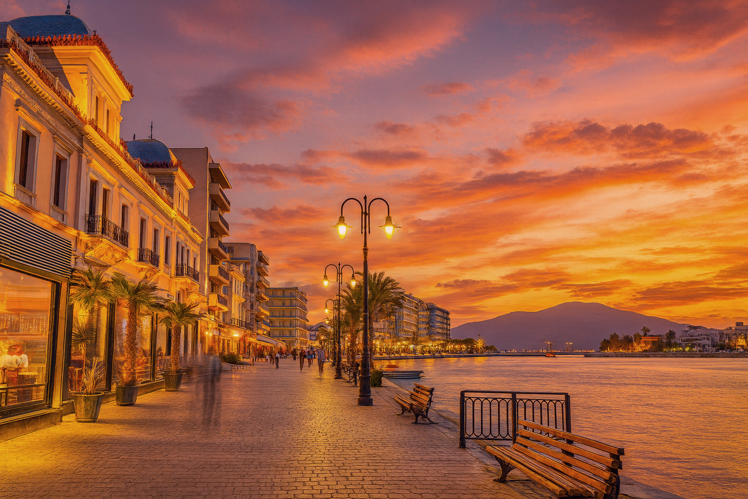 Abendstimmung an der Seepromenade in Chalkida mit beleuchteten Fassaden, malerischem Sonnenuntergangshimmel und Spaziergängern entlang der Uferpromenade.