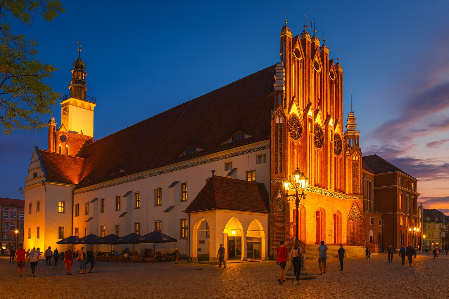 Abendstimmung am Rathaus in Frankfurt (Oder) mit beleuchteter Fassade und Spaziergängern auf dem Platz.