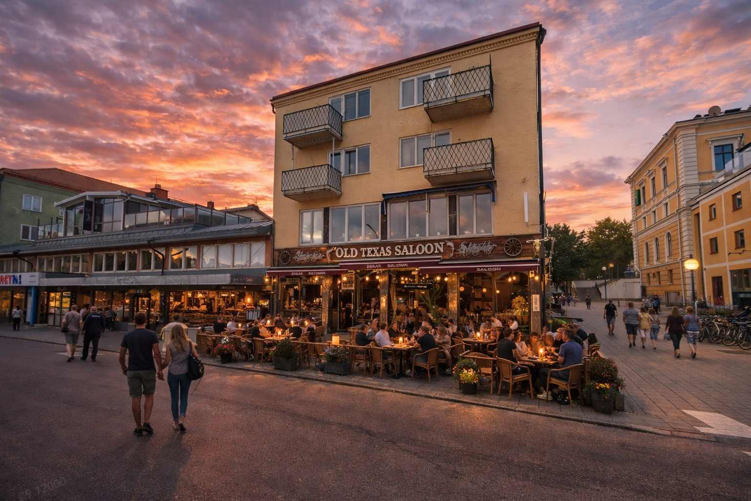 Hamngatan in Hudiksvall bei Sonnenuntergang mit Blick auf das Gebäude Old Texas Saloon, warm beleuchteten Fenstern und eingeschalteten Außenlampen, belebtem Straßencafé ohne Absperrungen mit vielen Gästen an Tischen und stimmungsvoller Beleuchtung sowie Spaziergängern entlang der Straße, goldene Abendstimmung unter einem orangefarbenen Wolkenhimmel