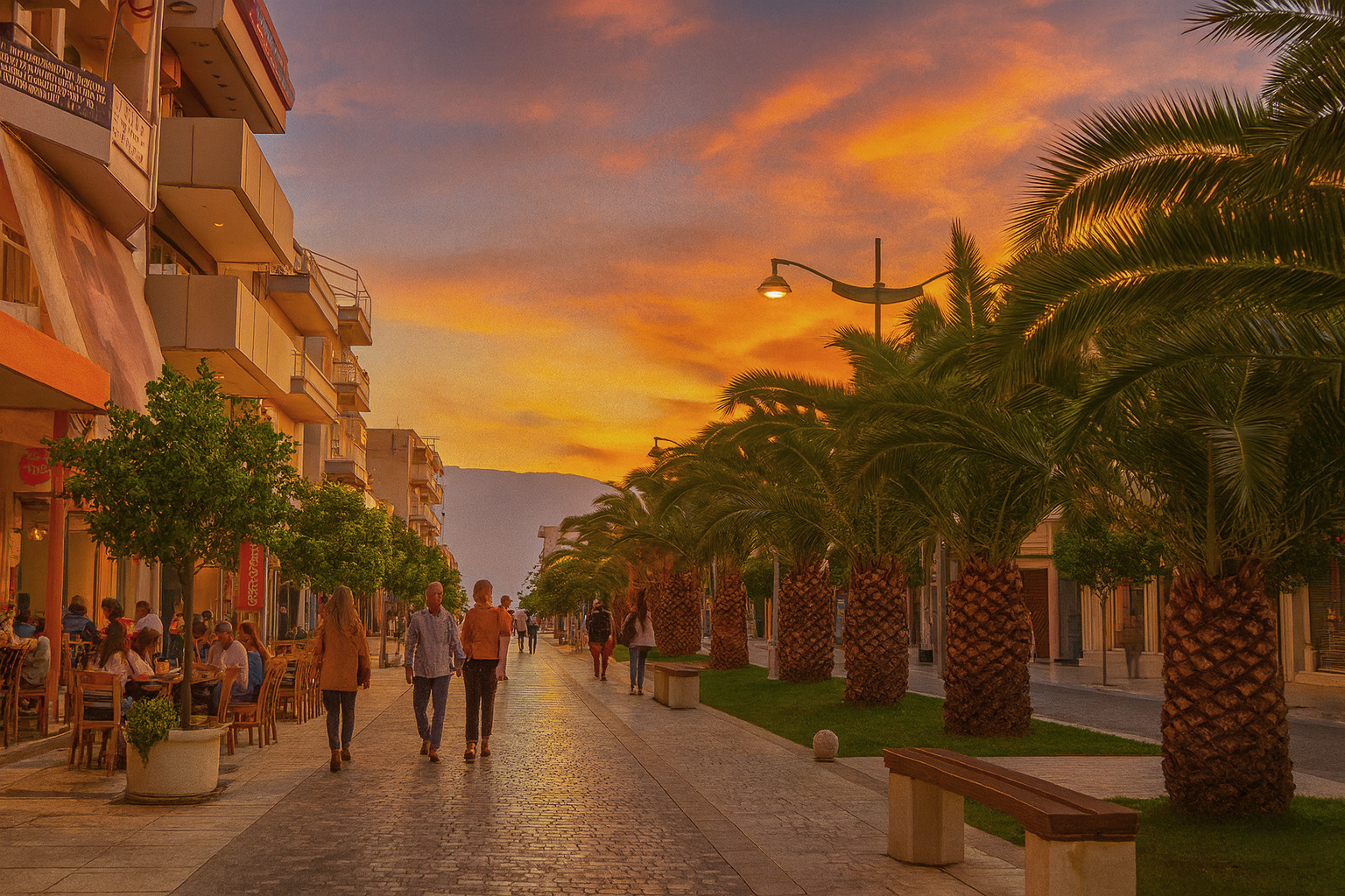 Abendstimmung in der Fußgängerzone von Korinth mit beleuchtetem Straßencafé, Palmen und Spaziergängern unter malerischem Sonnenuntergangshimmel.