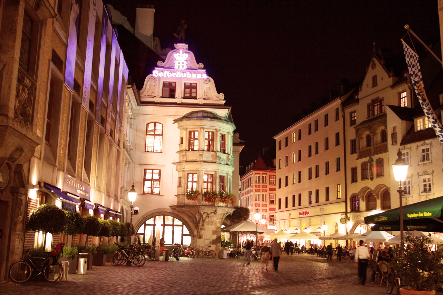 Abendstimmung in der Fußgängerzone von München am Hofbräuhaus mit beleuchtetem Straßencafé, erhellten Fassaden, Spaziergängern.