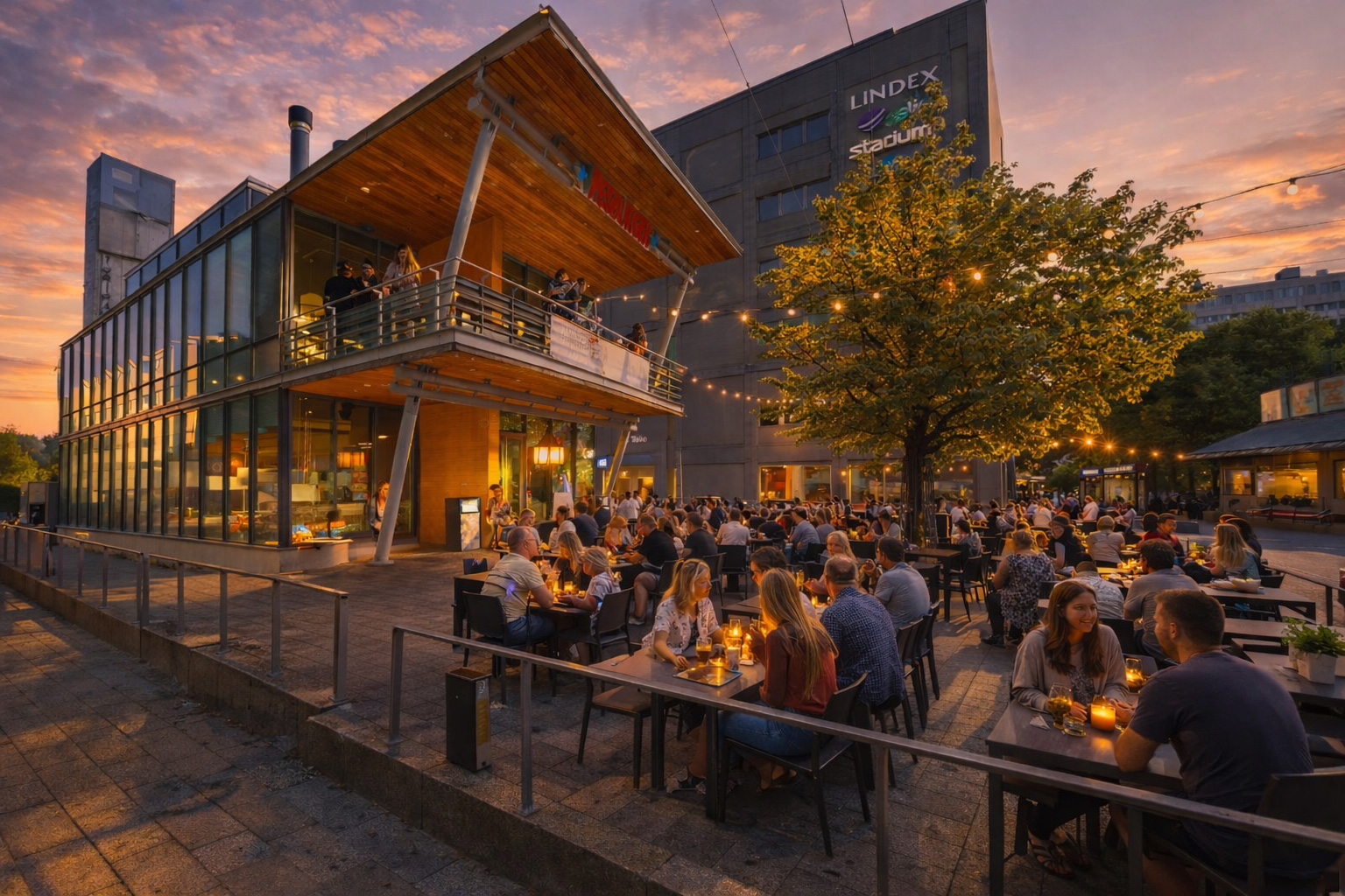 Belebtes Straßencafé bei Sonnenuntergang mit moderner Glasfassade, warm beleuchteten Innenräumen, Lichterketten im Baum und vielen Gästen an Tischen auf der Terrasse
