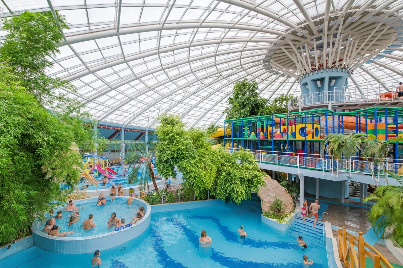 Aquaticum Spa in Debrecen mit tropischen Pflanzen und bunten Wasserrutschen unter einem großen Glasdach bei Sonnenlicht