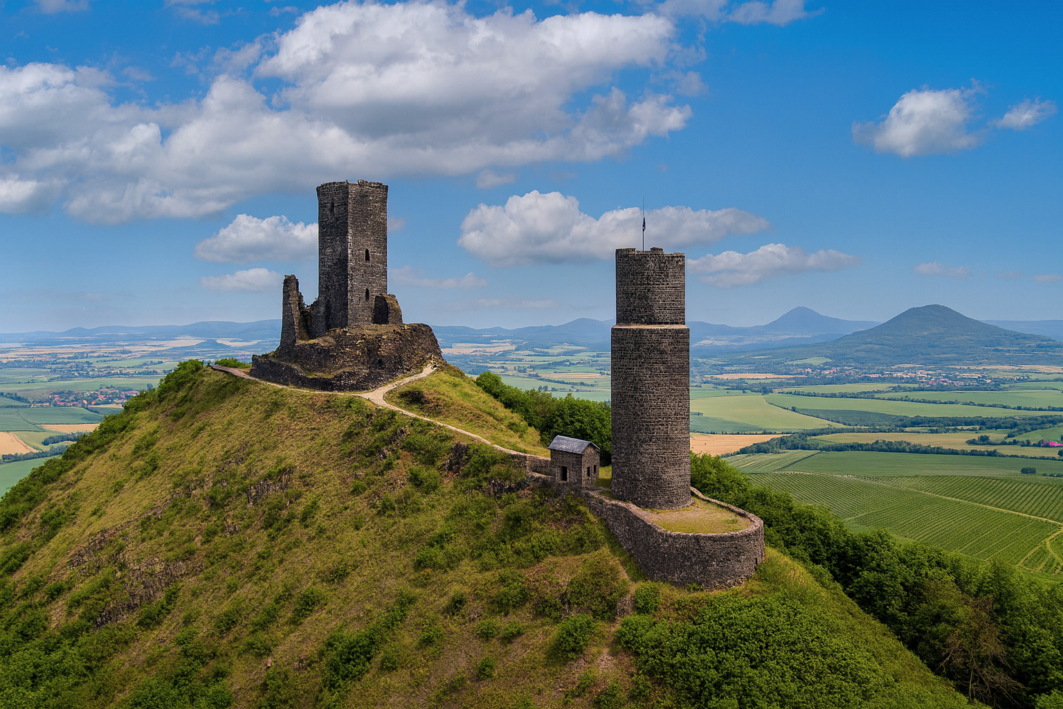 Burg Hazmburk auf einem Hügel mit malerischen weiß-grauen Wolken, sonniger Beleuchtung und weiter Aussicht auf das böhmische Umland