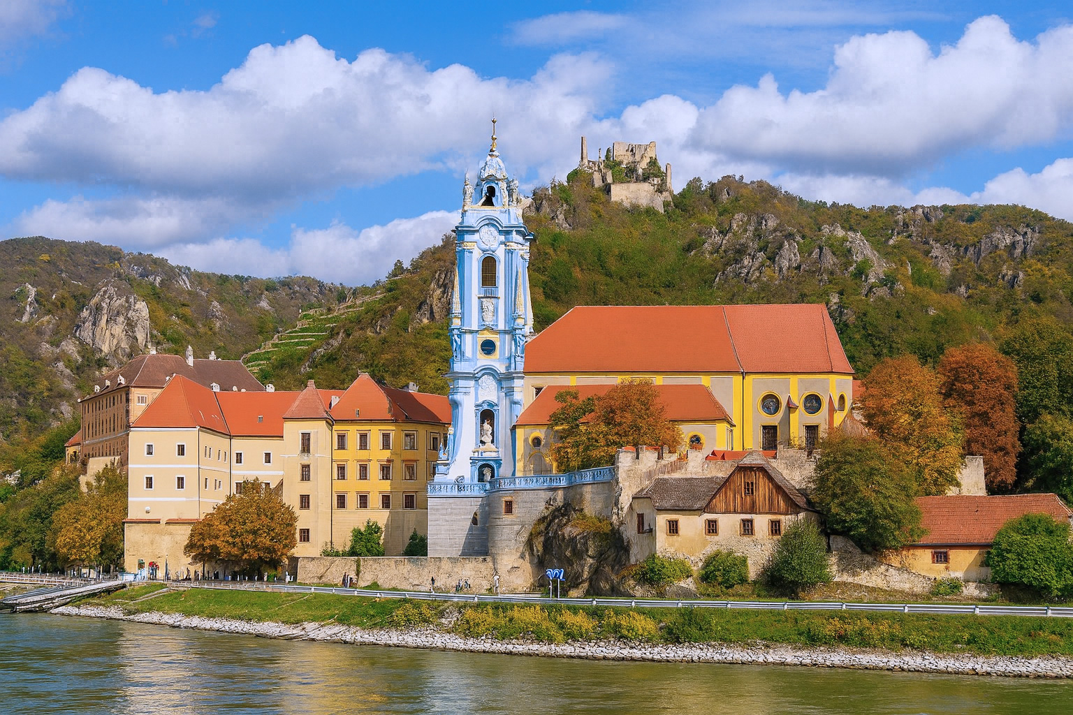 Dürnstein in der Wachau mit der blauen Stiftskirche und der Burgruine, unter malerischen weiß-grauen Wolken bei hellem Sonnenlicht