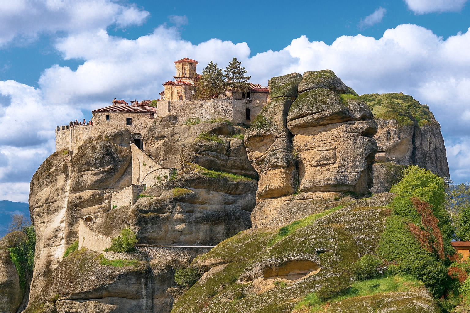 Das Kloster Varlaám in Meteora, Griechenland, thront auf einer steilen Felsformation unter weiß-grauen Wolken im besten Sonnenlicht.