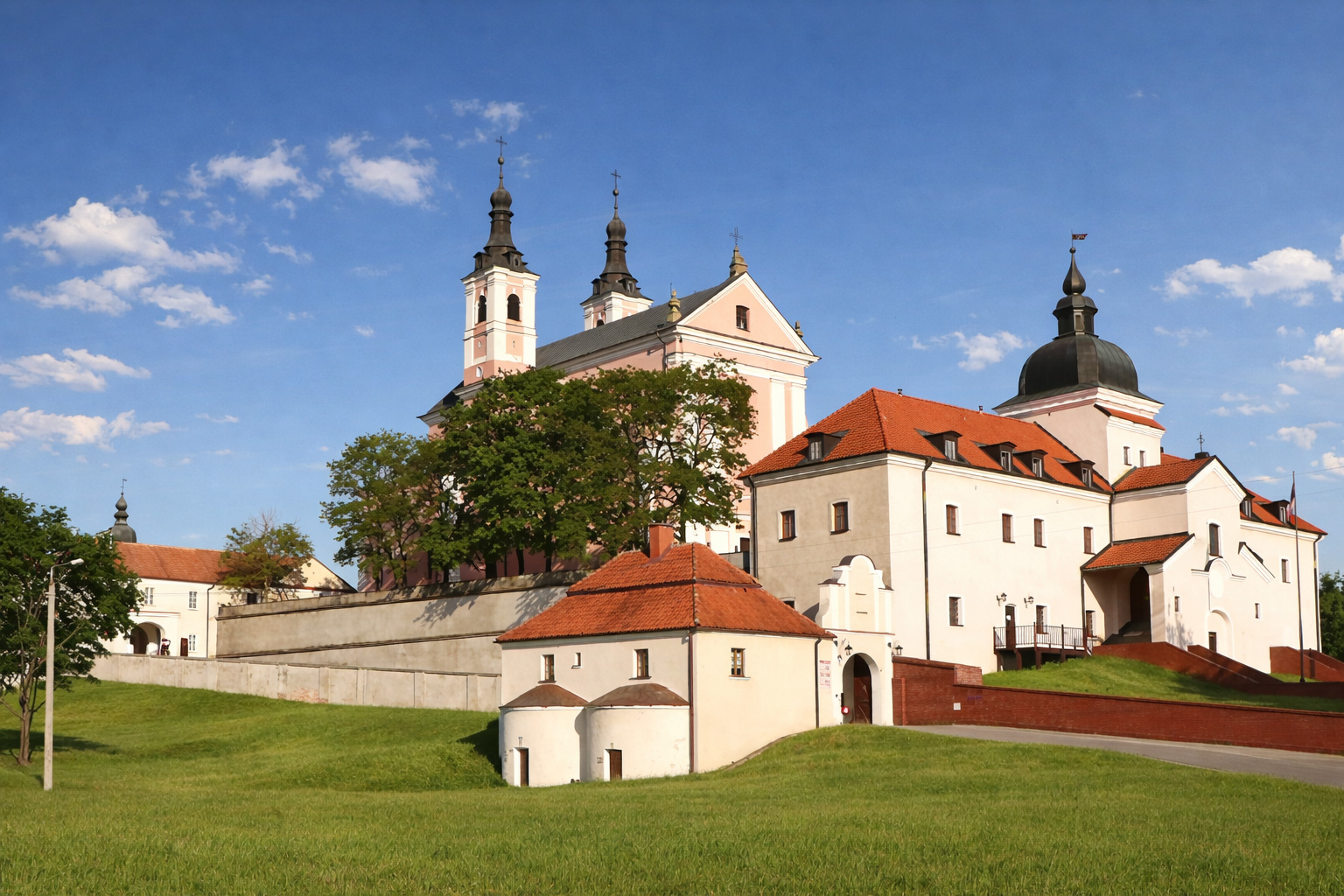 Klosteranlage Wigry auf einer Anhöhe mit barocker Kirche, weißen Gebäuden mit roten Dächern und gepflegten Wiesen unter klarem blauem Himmel