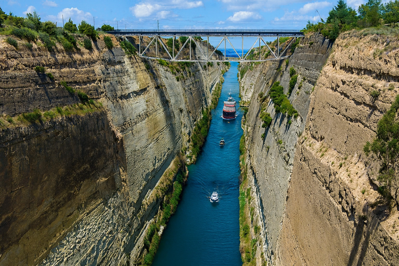 Der Korinthkanal in Griechenland mit steilen Felswänden und blauem Wasser unter malerischen weiß-grauen Wolken im besten Sonnenlicht, ein Schiff fährt durch den Kanal.