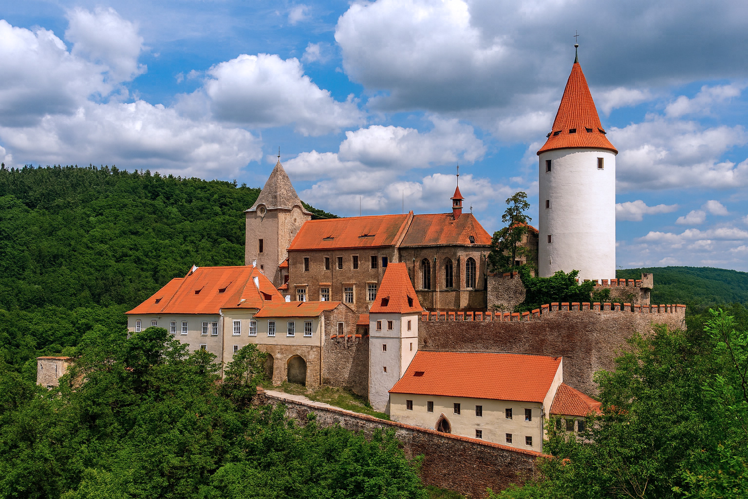 Burg Křivoklát mit malerischen weiß-grauen Wolken, sonniger Beleuchtung und rotem Ziegeldach