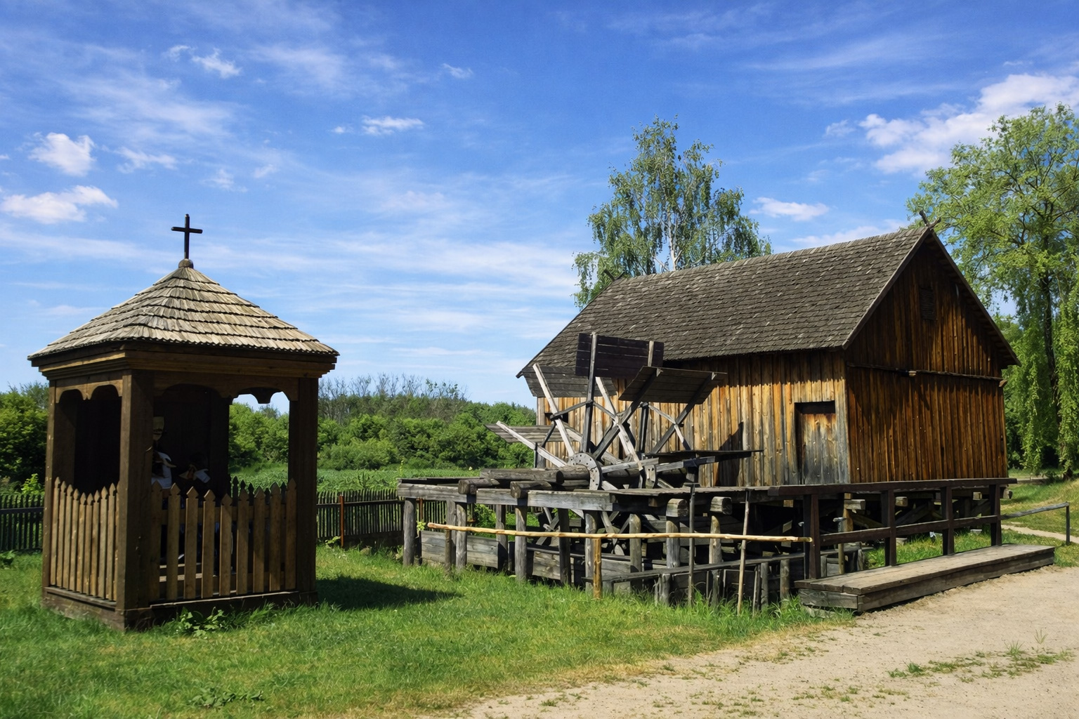 Historische Holzbauten im Kurpie-Freilichtmuseum mit kleiner Kapelle, alter Mühle, Wiese und sandigem Weg unter leicht bewölktem Himmel