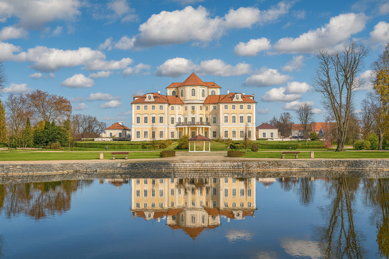 Schloss Liblice mit malerischen weiß-grauen Wolken, sonniger Beleuchtung und Spiegelung im Teich