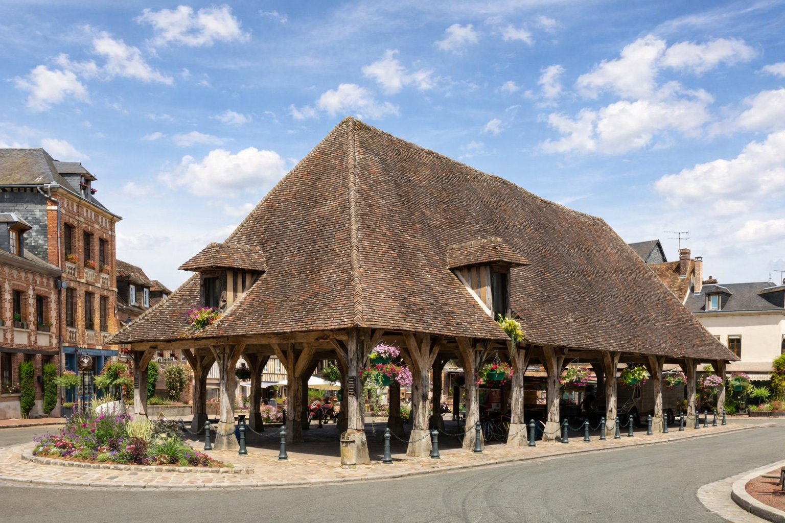 Historische Markthalle aus Holz mit großem Ziegeldach in Lyons-la-Forêt, blumengeschmückte Balken und ruhiger Platz mit umliegenden Fachwerk- und Backsteinhäusern unter hellem Himmel