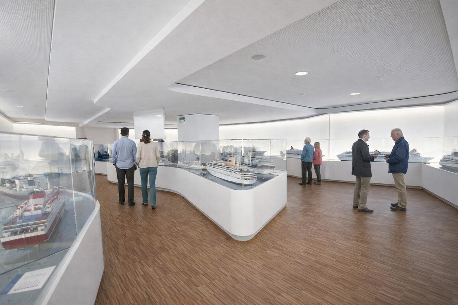 Heller Ausstellungsraum im Meyer Werft Besucherzentrum mit detailreichen Schiffsmodellen in Glasvitrinen, Besucher betrachten moderne Kreuzfahrtschiffe in maritimer Ausstellung mit Holzfußboden und klarer Architektur