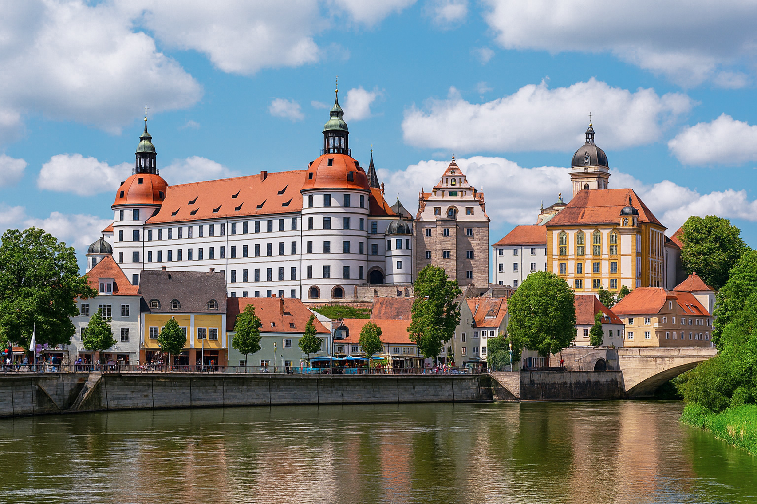 Schloss Neuburg an der Donau mit malerischen weiß-grauen Wolken, sonniger Beleuchtung und Reflexion im Fluss