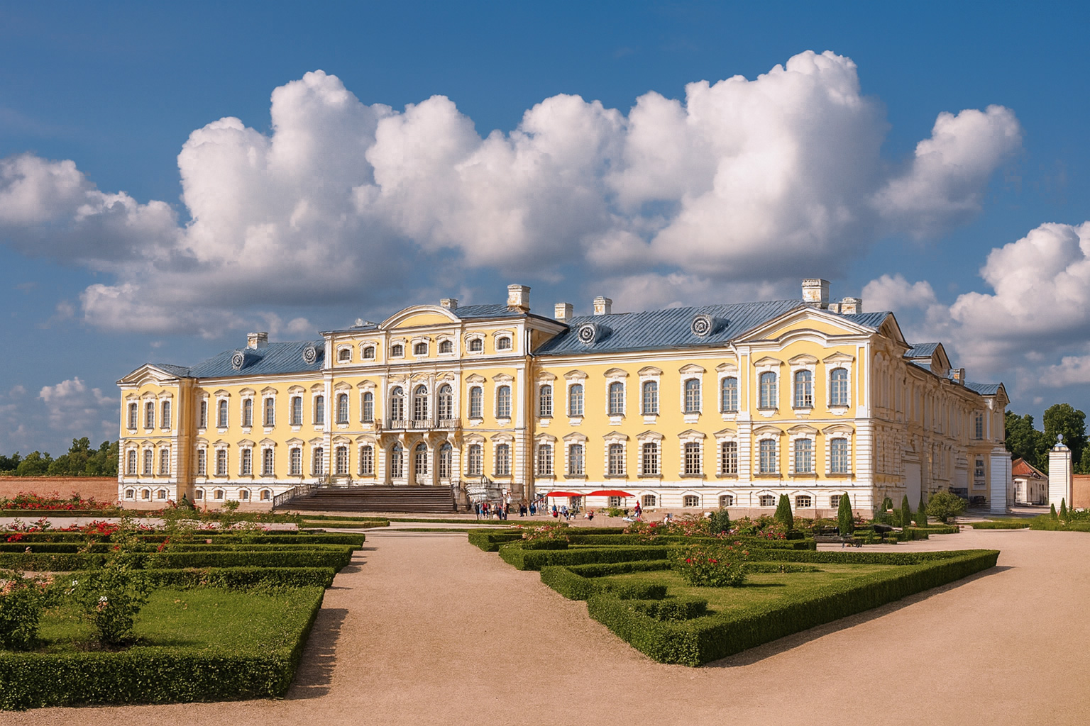 Rundale Palace bei Bauska in Lettland mit barocker Fassade und gepflegtem Schlossgarten unter blauem Himmel mit malerischen weiß-grauen Wolken im Sonnenschein.