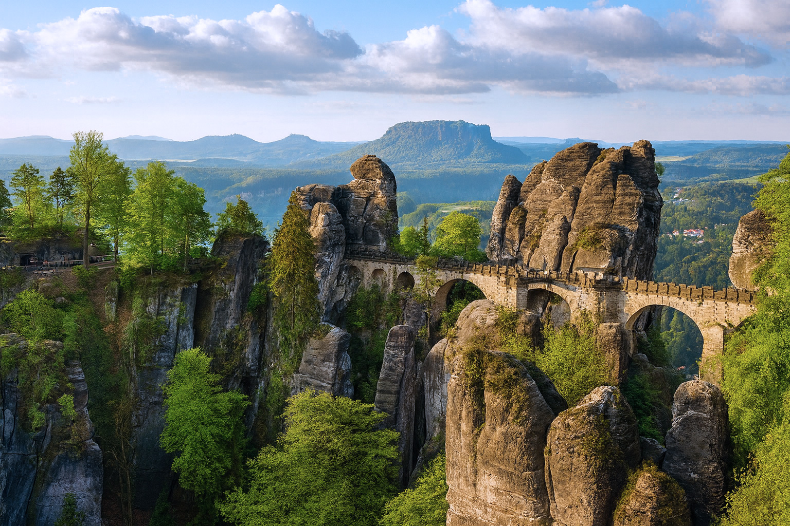Basteibrücke in der Sächsischen Schweiz mit malerischen weiß-grauen Wolken, grünen Felsen und weichem Sonnenlicht