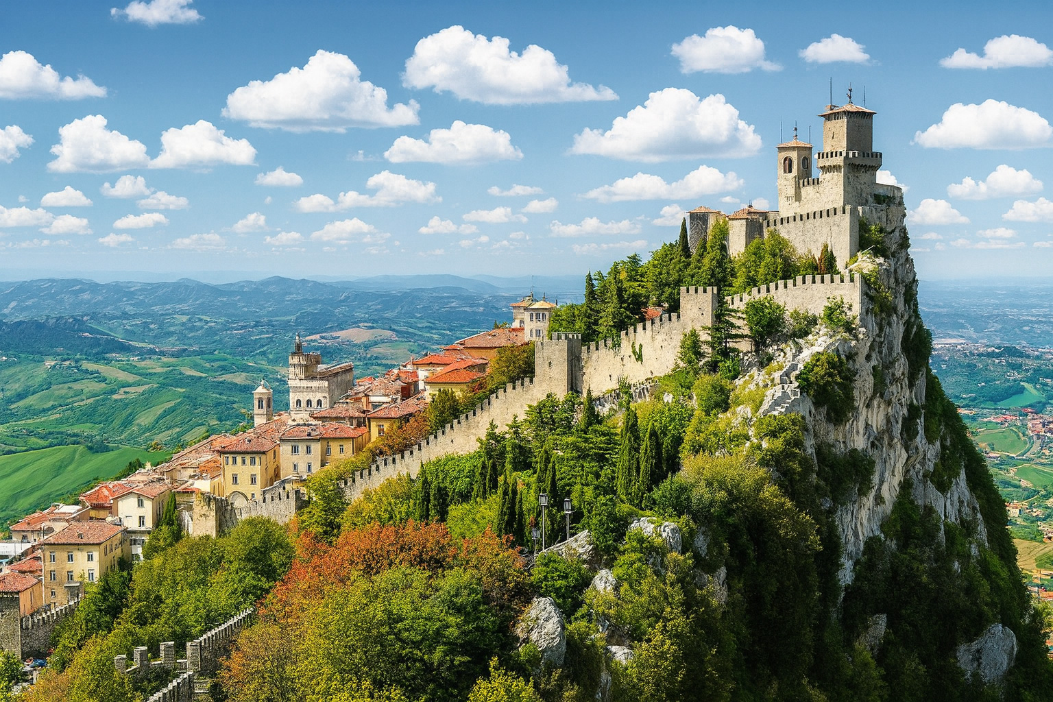 Festung Guaita in San Marino auf dem Monte Titano mit Blick über die Altstadt und die grünen Hügel bei blauem Himmel mit weißen Wolken.