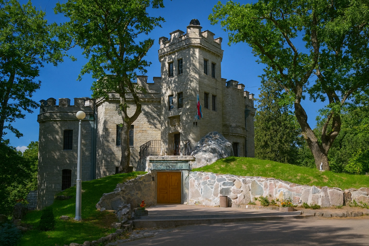 Schloss Hohenhaupt bei Tallinn aus hellem Stein unter klarem blauem Himmel im Sonnenschein, umgeben von grünen Bäumen und gepflegtem Rasen.
