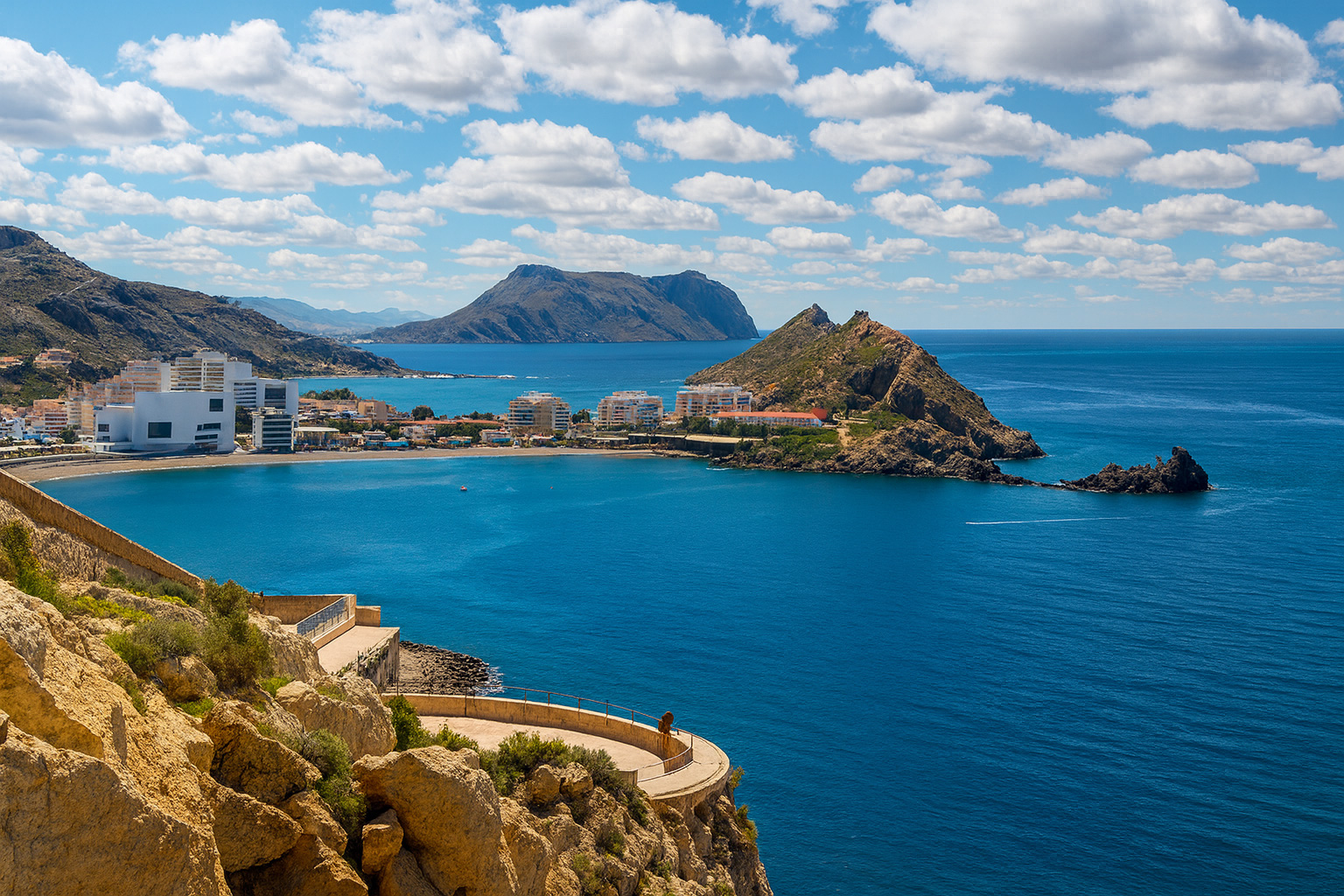 Panoramablick auf die Bucht von Águilas mit dem Aussichtspunkt und malerischen weiß-grauen Wolken über dem tiefblauen Mittelmeer.