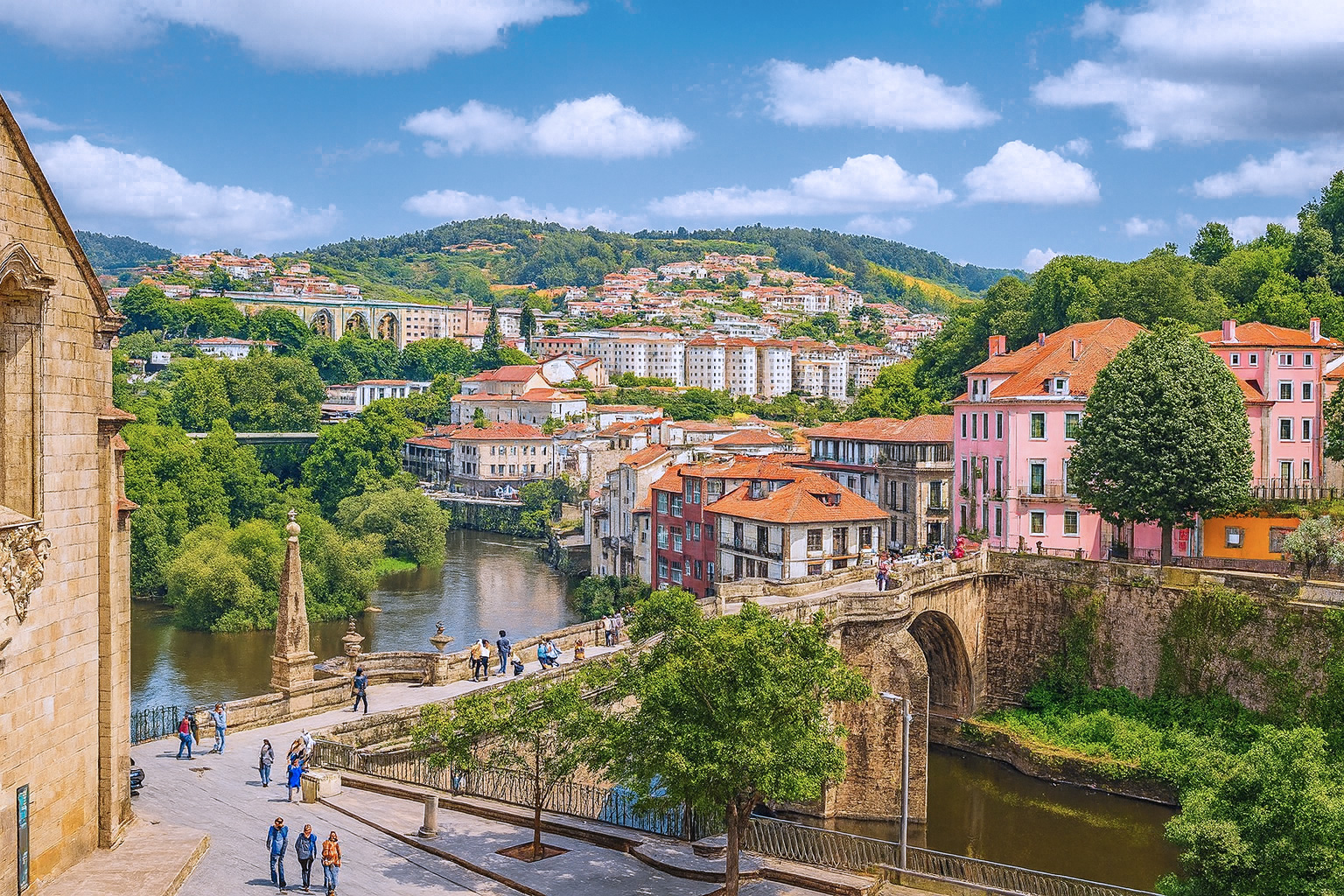 Panoramaaufnahme von Amarante in Portugal mit der Ponte de São Gonçalo Brücke über den Fluss Tâmega, umgeben von bunten Häusern und grünen Hügeln bei klarem Sonnenlicht und malerischen weiß-grauen Wolken.