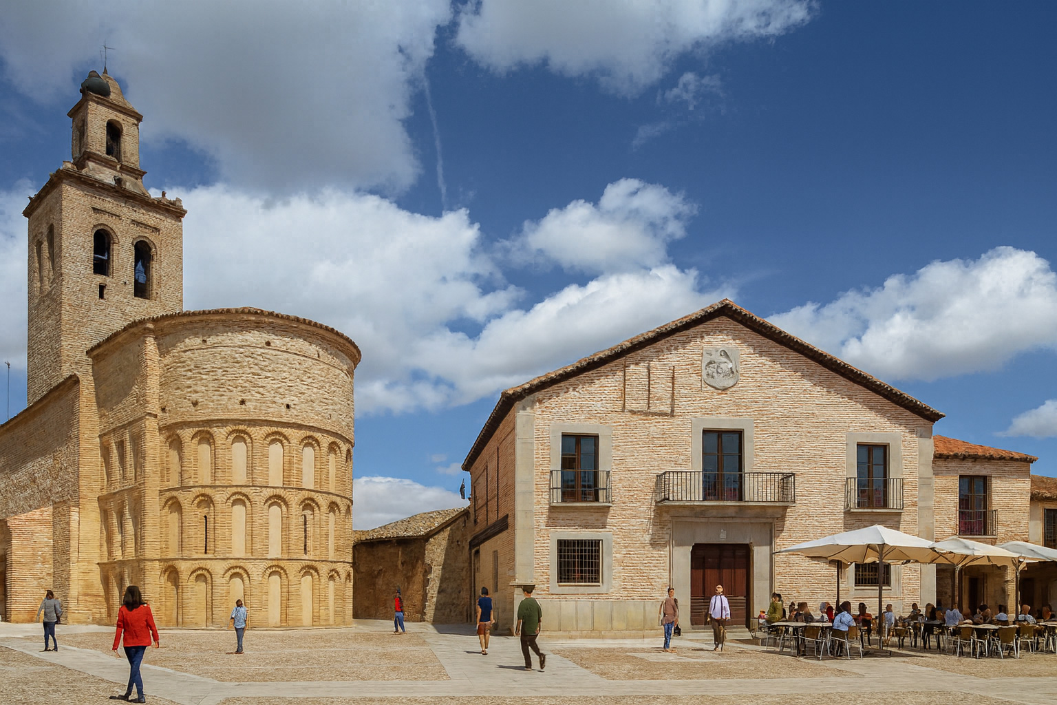 Plaza de la Villa in Arévalo mit der Santa Maria Kirche, einem Straßencafé und Spaziergängern bei klarem Sonnenlicht und malerischen weiß-grauen Wolken.