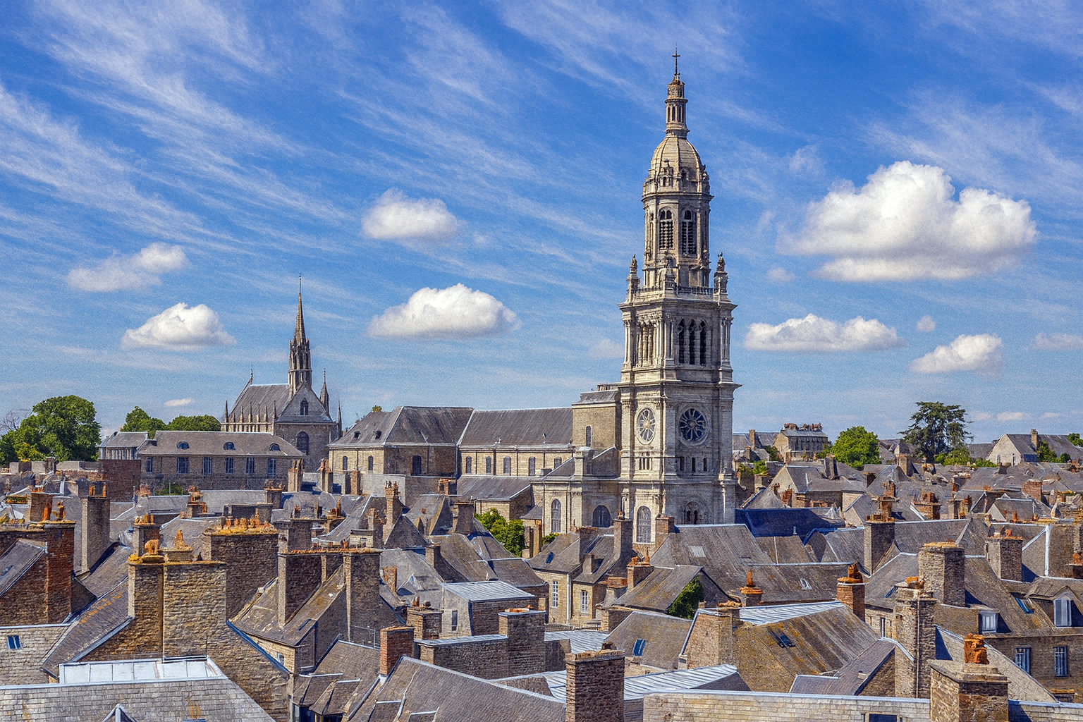 Panorama über die Dächer der Altstadt von Avranches mit der Basilique Saint-Gervais d’Avranches im Hintergrund unter malerischen weiß-grauen Wolken im besten Sonnenlicht.