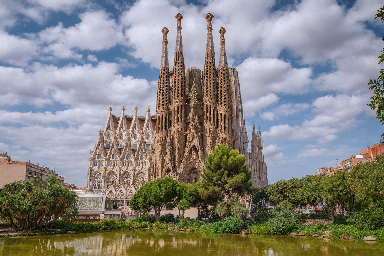 Die Sagrada Família Kathedrale in Barcelona mit dem Plaça de Gaudí Park im vordergrund unter malerischen weiß-grauen Wolken im besten Sonnenlicht.