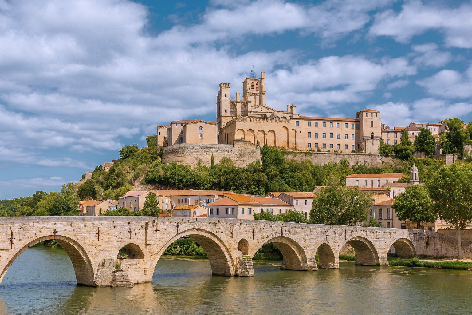 Die Pont Vieux Brücke in Béziers mit der Kathedrale Saint-Nazaire im Hintergrund unter malerischen weiß-grauen Wolken im besten Sonnenlicht.