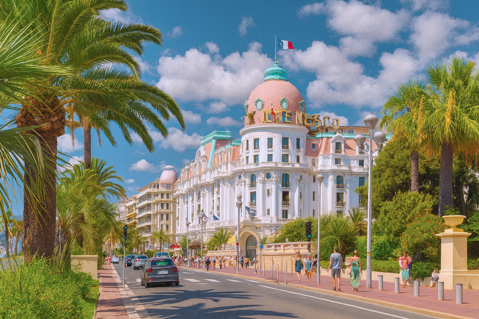 Le Negresco Hotel an der Strandpromenade in Cannes mit Palmenallee und malerischen weiß-grauen Wolken im sonnigen Himmel.