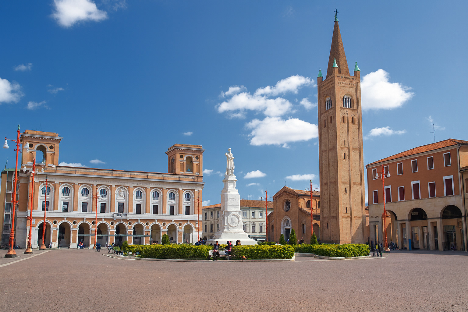 Piazza Saffi in Forlì mit der Statue von Aurelio Saffi, dem Campanile di San Mercuriale und historischen Gebäuden bei blauem Himmel mit weißen Wolken.