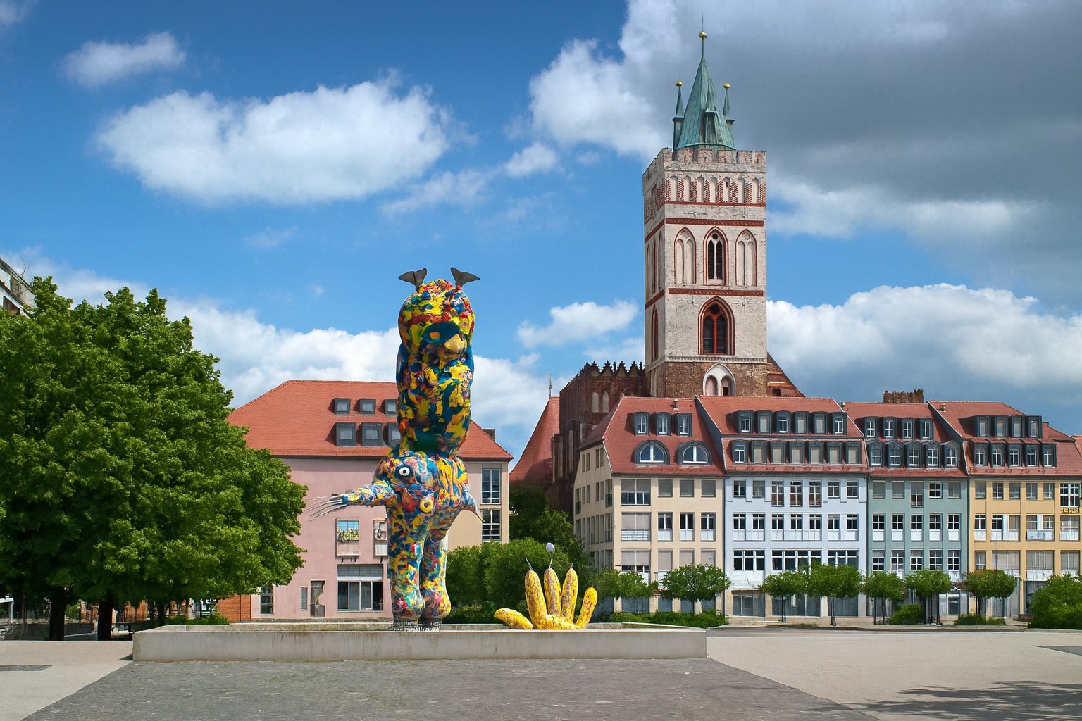 Comic Brunnen in Frankfurt (Oder) in Deutschland mit der St. Marienkirche im Hintergrund, bei Sonnenschein und malerischen Wolken.