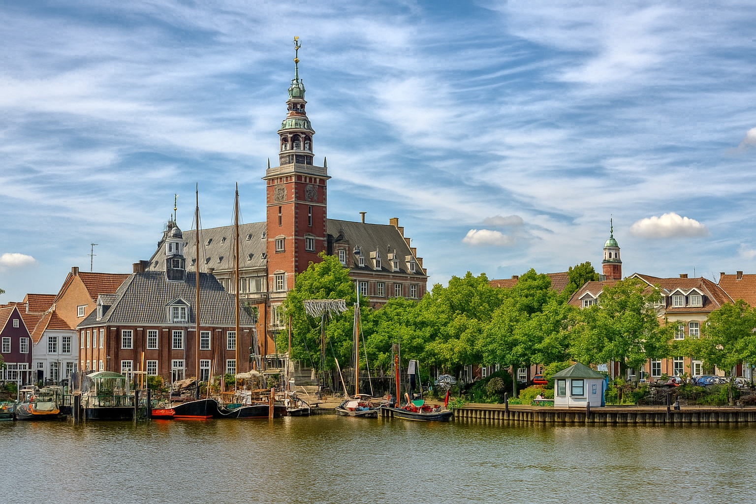 Panorama der Altstadt von Leer am Leda-Kanal mit dem historischen Rathaus und Segelbooten unter einem Himmel mit Zirrus- und Kumuluswolken.