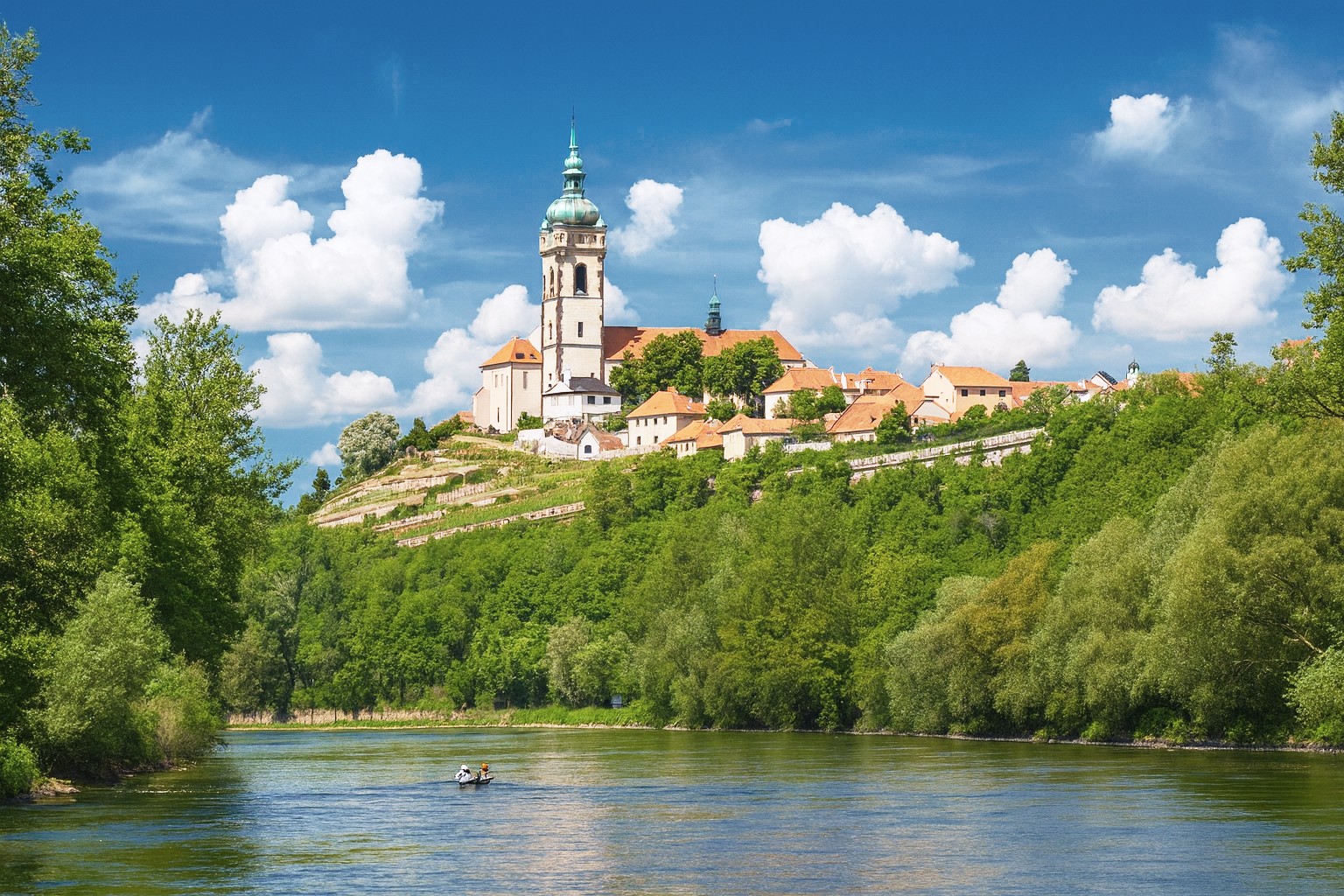 Stadt Mělník in Tschechien mit Kirche St. Peter und Paul auf einem Hügel an der Elbe, bei strahlender Mittagssonne mit malerischen weißen Wolken am blauen Himmel.