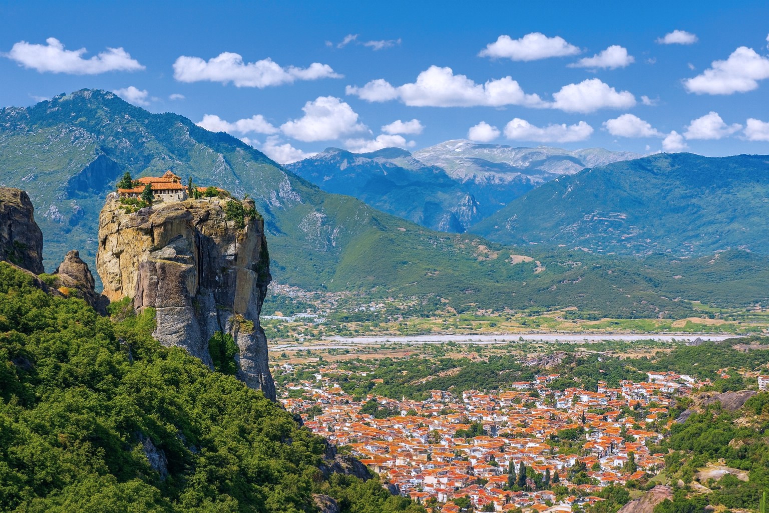 Panoramaaufnahme des Meteora-Klosters bei Kalambaka in Griechenland mit markantem Felsen, Klosteranlage und weißen Wolken über den Bergen.