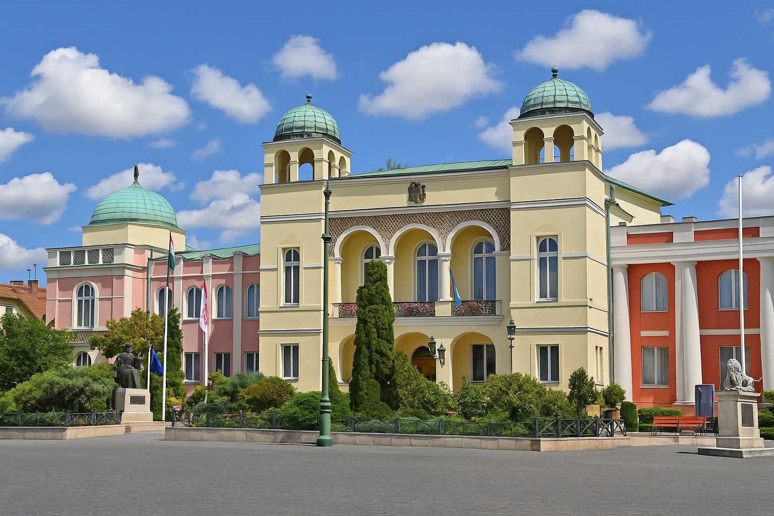 Rathaus von Mohács in Ungarn mit Kuppeln und farbiger Fassade bei blauem Himmel mit weißen Wolken.