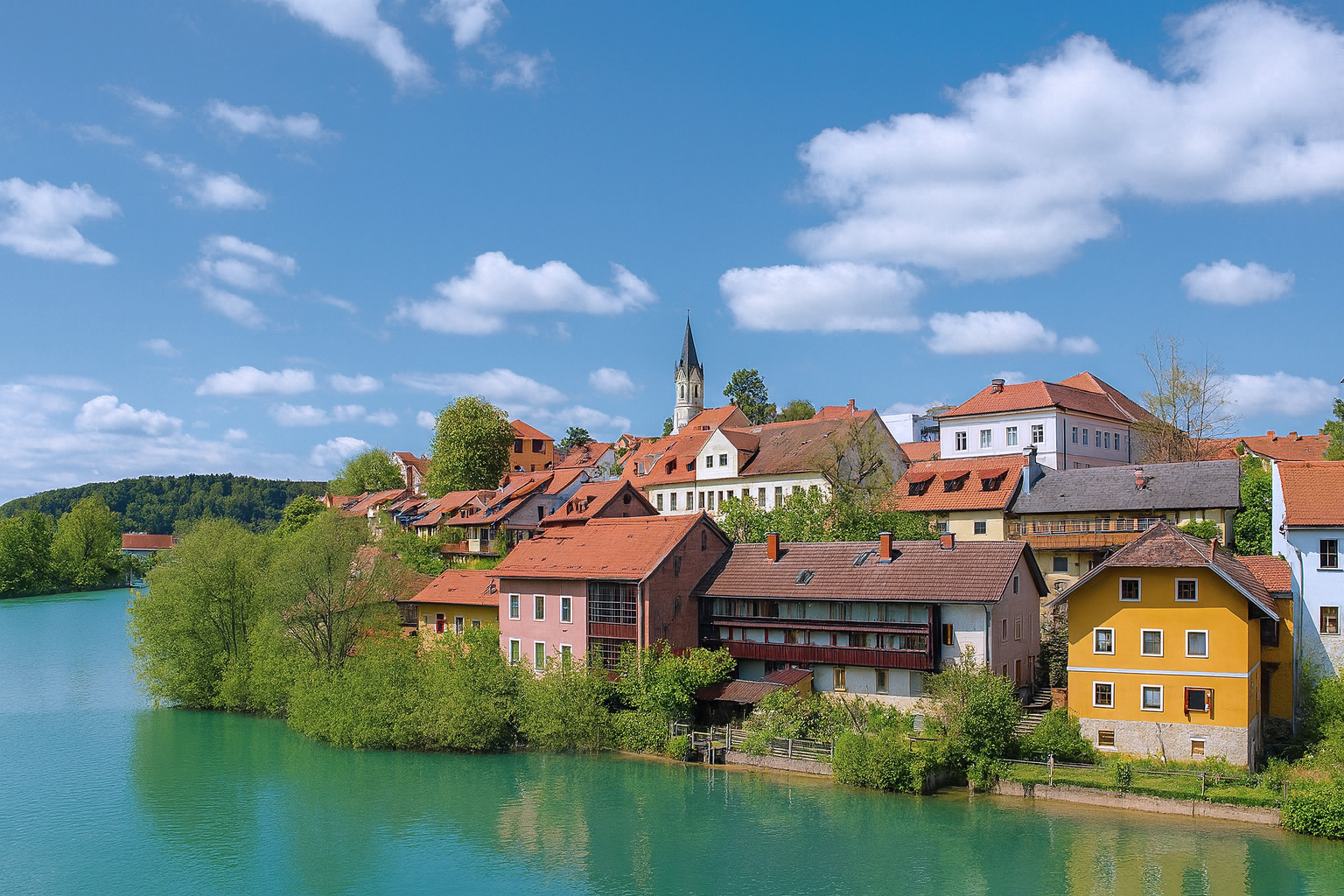 Altstadt von Novo mesto in Slowenien mit roten Ziegeldächern am Ufer der Krka bei blauem Himmel und weißen Wolken.