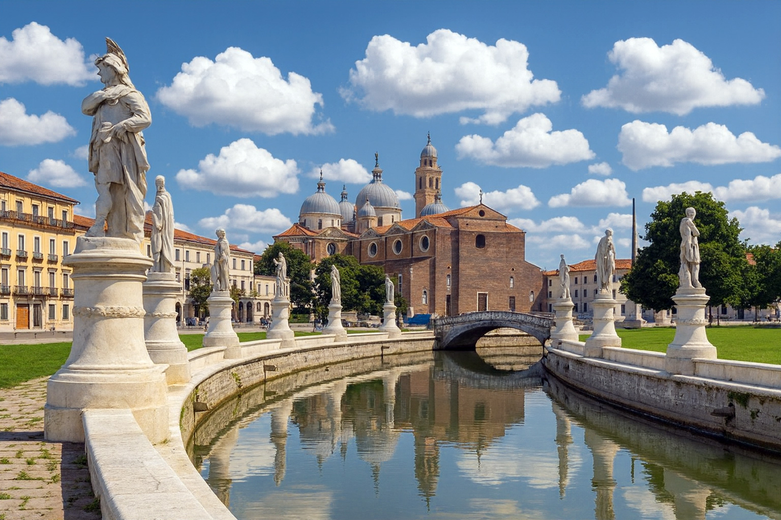 Prato della Valle in Padua mit der Basilika Santa Giustina, Statuen entlang des Kanals und blauem Himmel mit weißen Wolken.