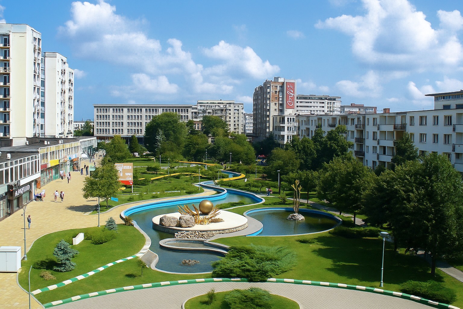 Zentralpark in Pitești mit goldenem Brunnen, Wasserläufen, Grünanlagen und Spaziergängern bei sonnigem Himmel mit weißen Wolken.