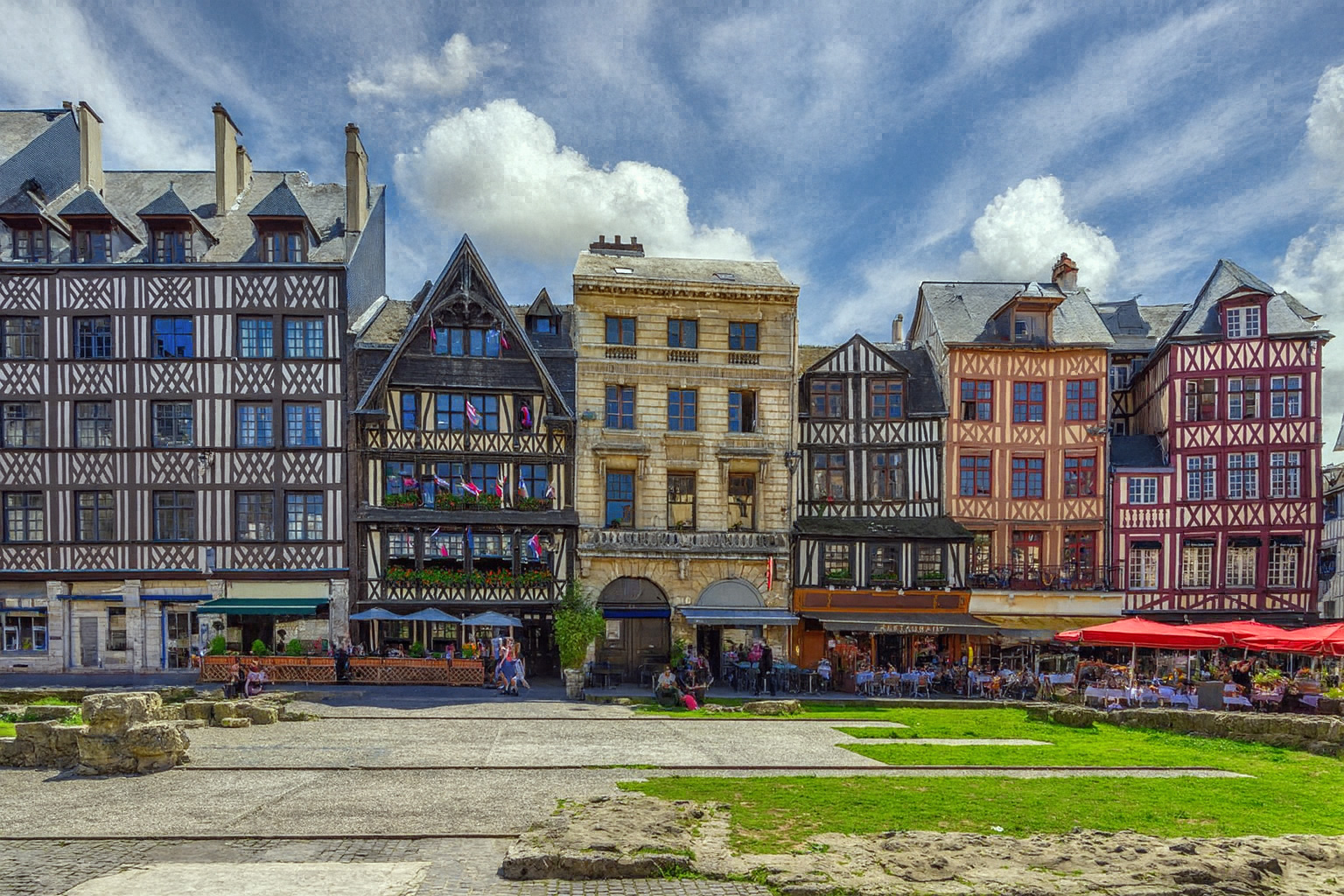 Panorama des Platzes an der Ruine der Kirche Saint-Sauveur in Rouen mit historischen Fachwerkhäusern und Straßencafés unter einem Himmel mit Zirrus- und Cumuluswolken bei Sonnenlicht.