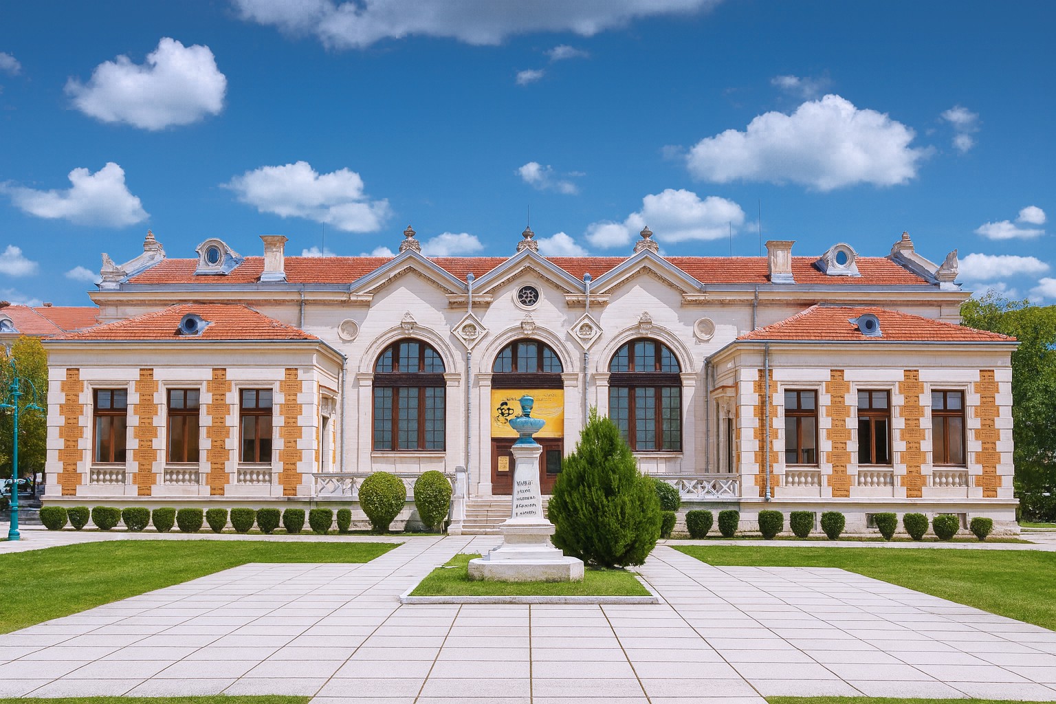 Madara Riser Gebäude in Schumen mit neuwertigen Bodenplatten, gepflegtem Vorplatz und blauem Himmel mit weißen Wolken.