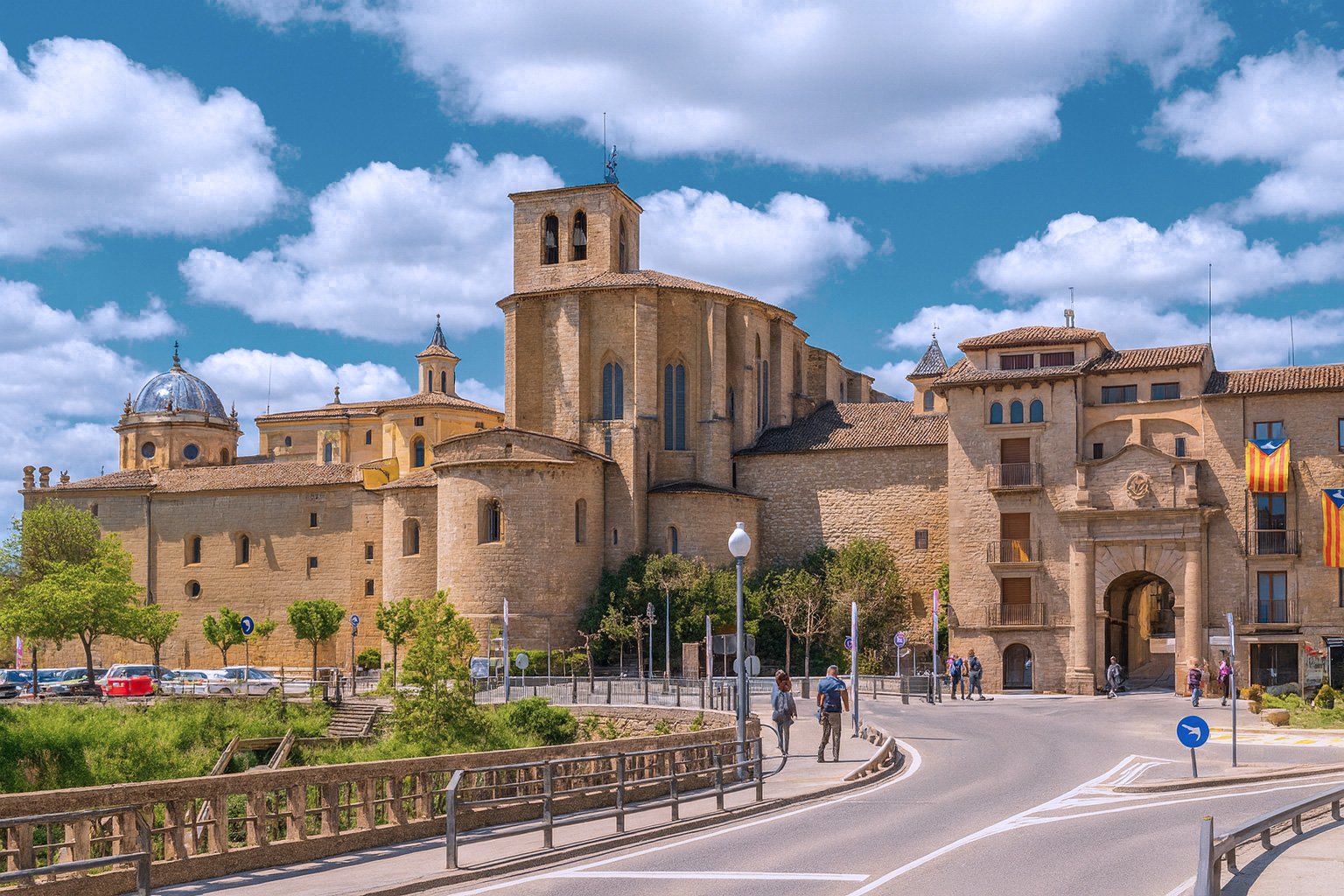 Tor zur Altstadt von Solsona mit der Kathedrale Santa Maria unter malerischen weiß-grauen Wolken im warmen Sonnenlicht.