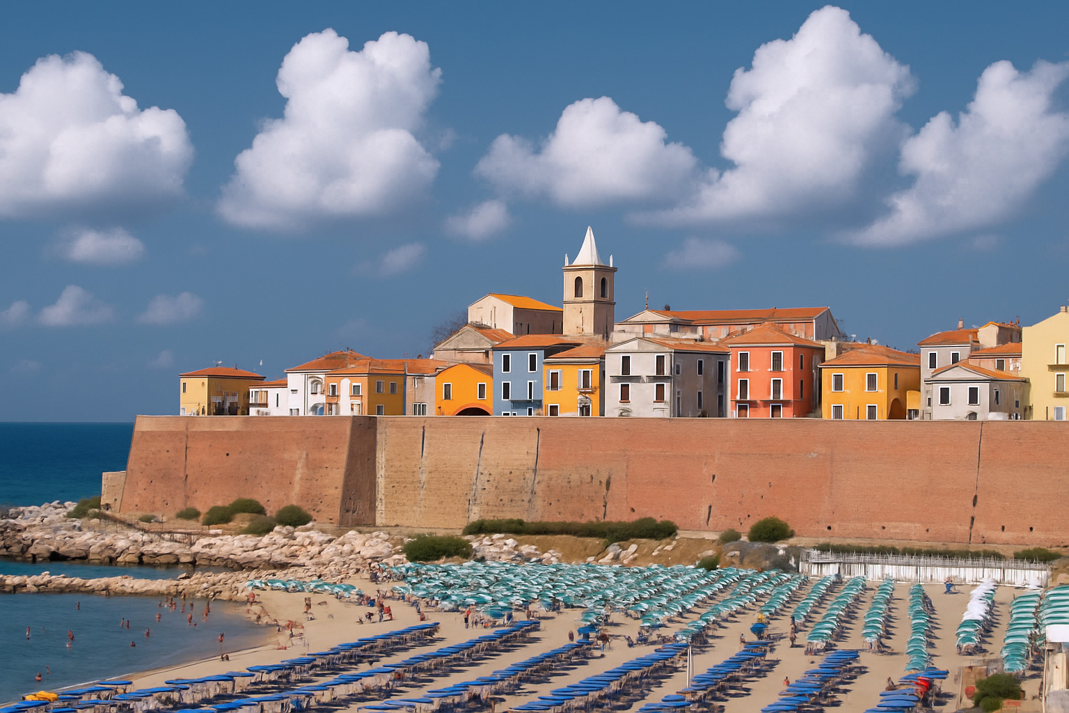 Altstadt von Termoli mit bunten Häusern über dem Strand und variierenden weiß-grauen Wolken im warmen Sonnenlicht.
