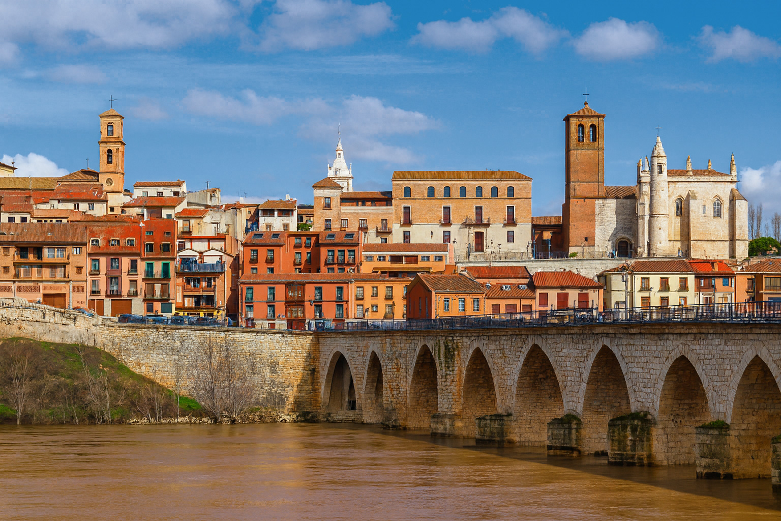 Panorama der Altstadt von Tordesillas mit der alten Steinbrücke über den Douro-Fluss bei Sonnenlicht und malerischen weiß-grauen Wolken.