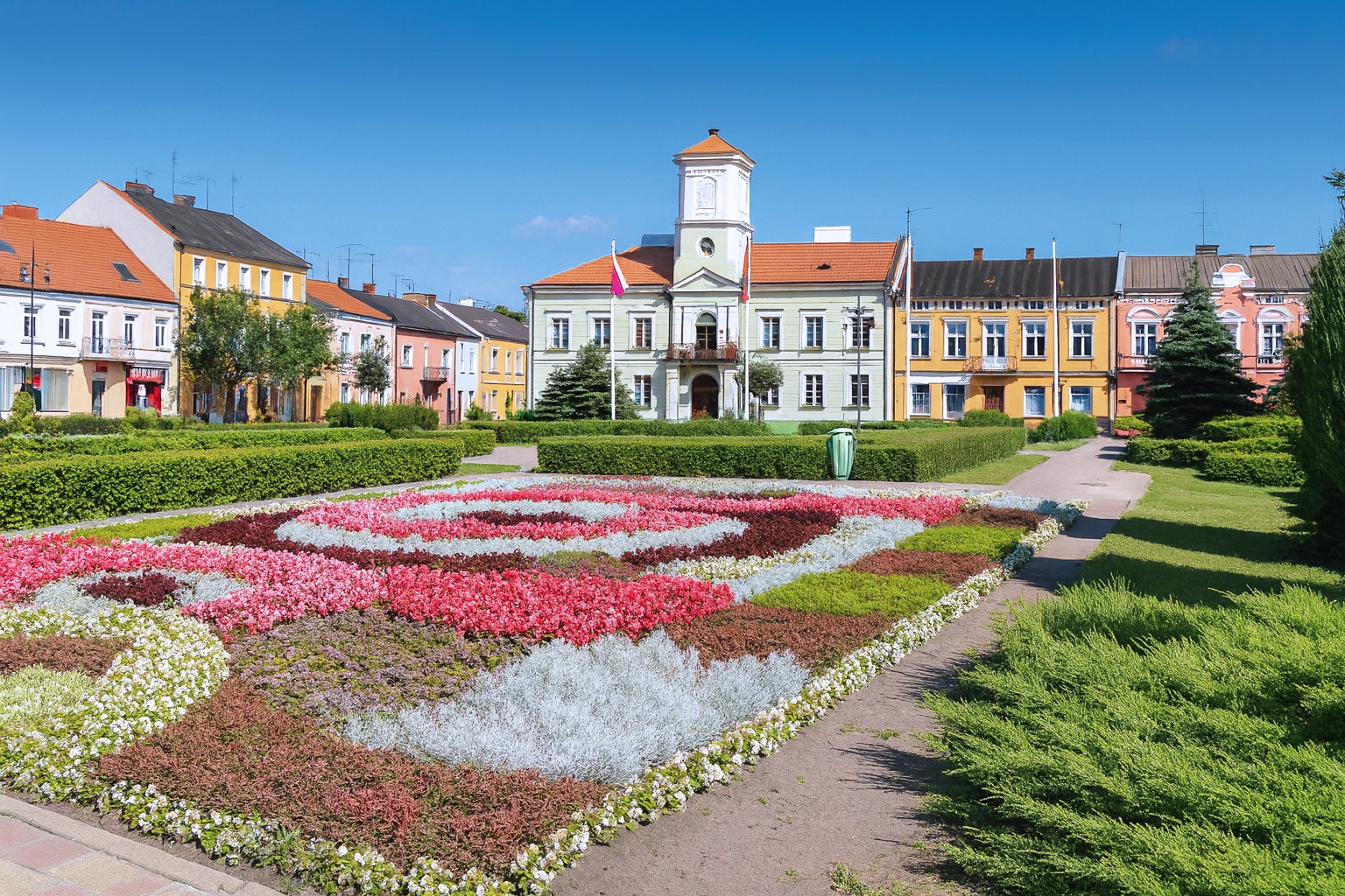 Plac Wojska Polskiego in Turek in Polen mit farbenfrohen Blumenbeeten und dem historischen Rathaus im Hintergrund.