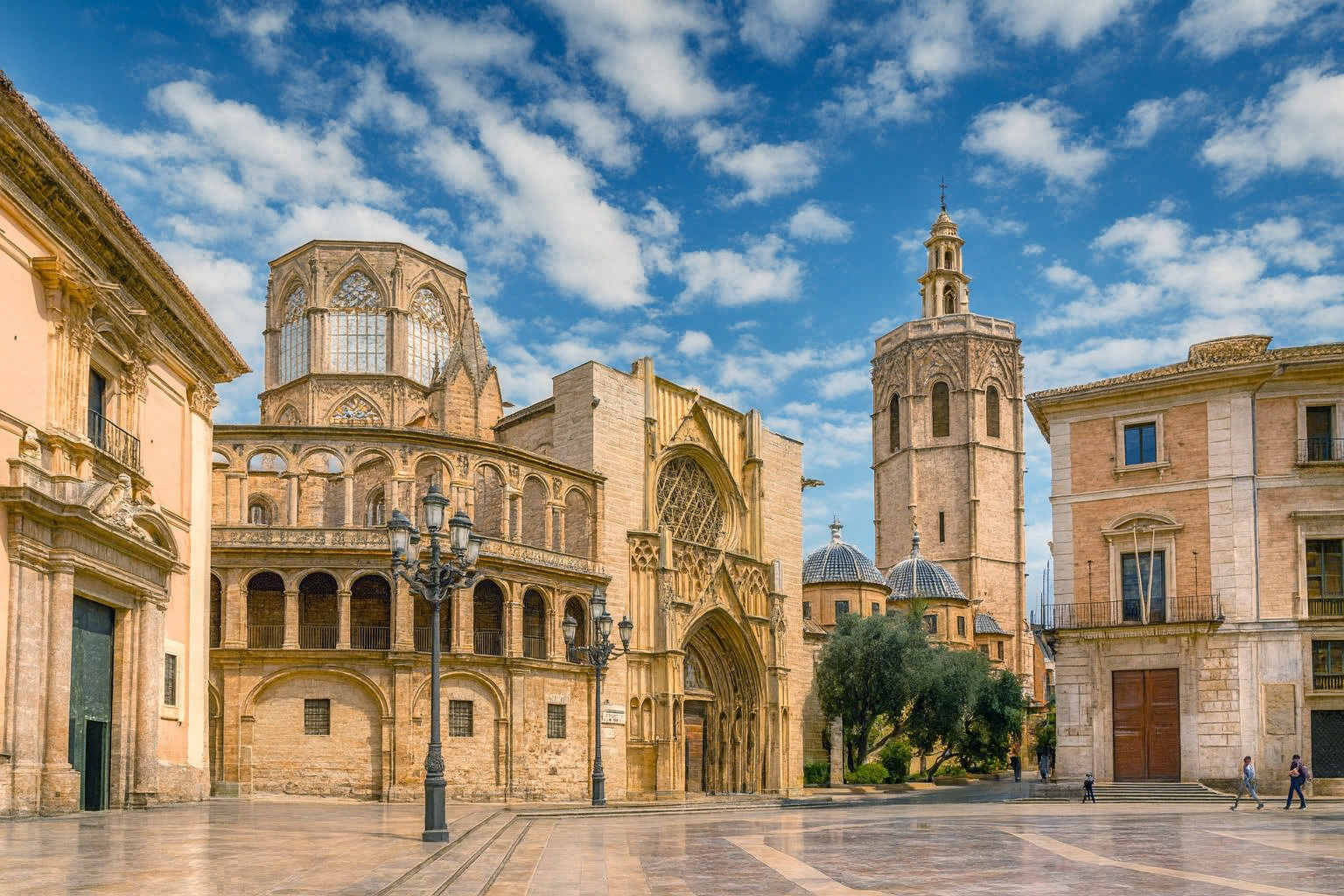 Kathedrale von Valencia mit dem Glockenturm El Miguelete unter malerischen weiß-grauen Wolken im warmen Sonnenlicht.