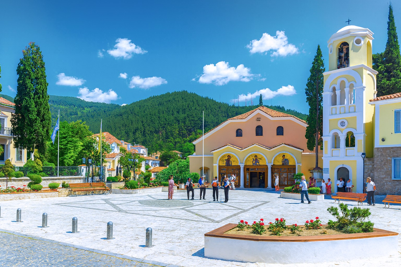 Mitropoleos-Platz in Xanthi mit der Metropolis-Kirche, griechischen Musikern in traditioneller Kleidung und Zuschauern bei sonnigem Himmel mit weißen Wolken.
