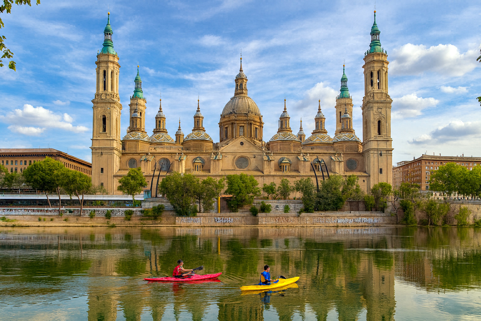 Basílica del Pilar in Saragossa mit Spiegelung im Ebro-Fluss, zwei Kanufahrer auf dem Wasser, unter blauem Himmel mit weißen Wolken bei warmem Sonnenlicht.