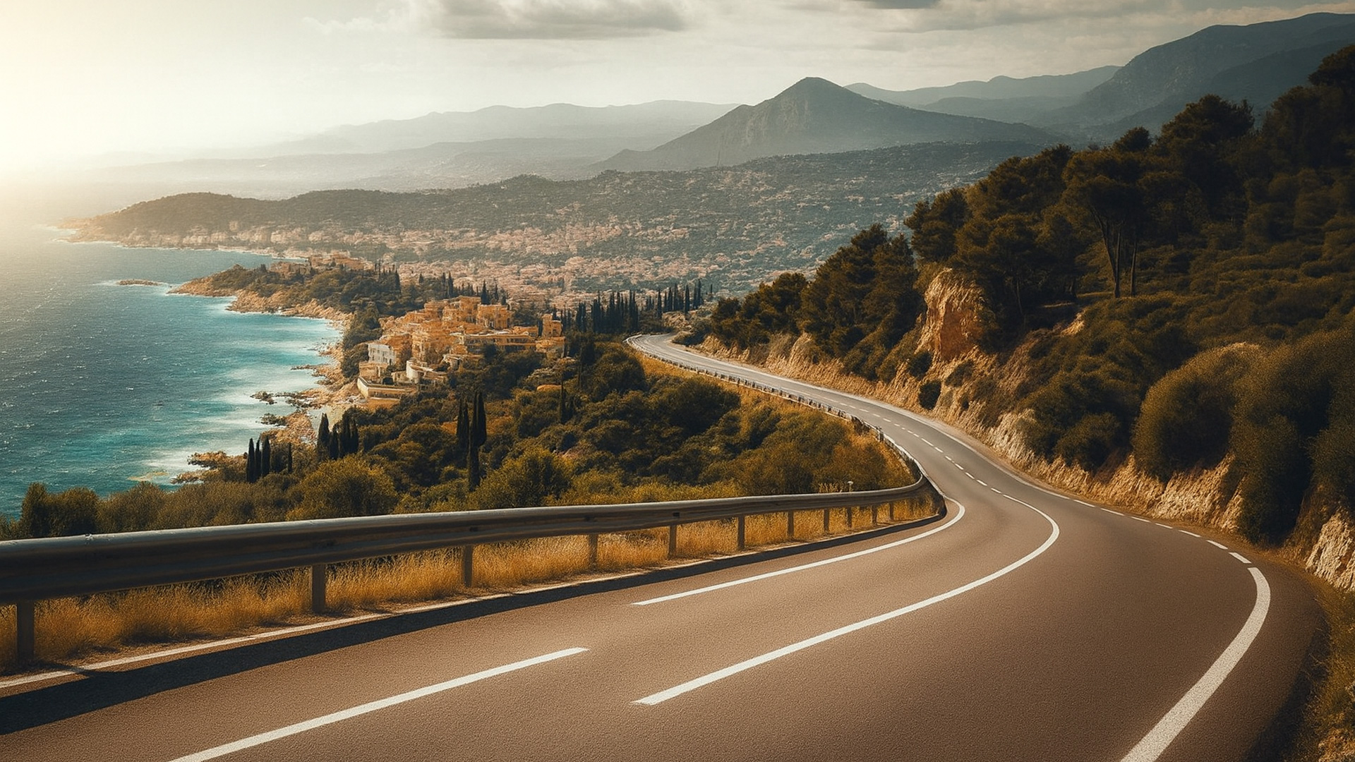 Kurvige Küstenstraße an der französischen Riviera mit Blick auf das Mittelmeer und ein mediterranes Dorf im Abendlicht.
