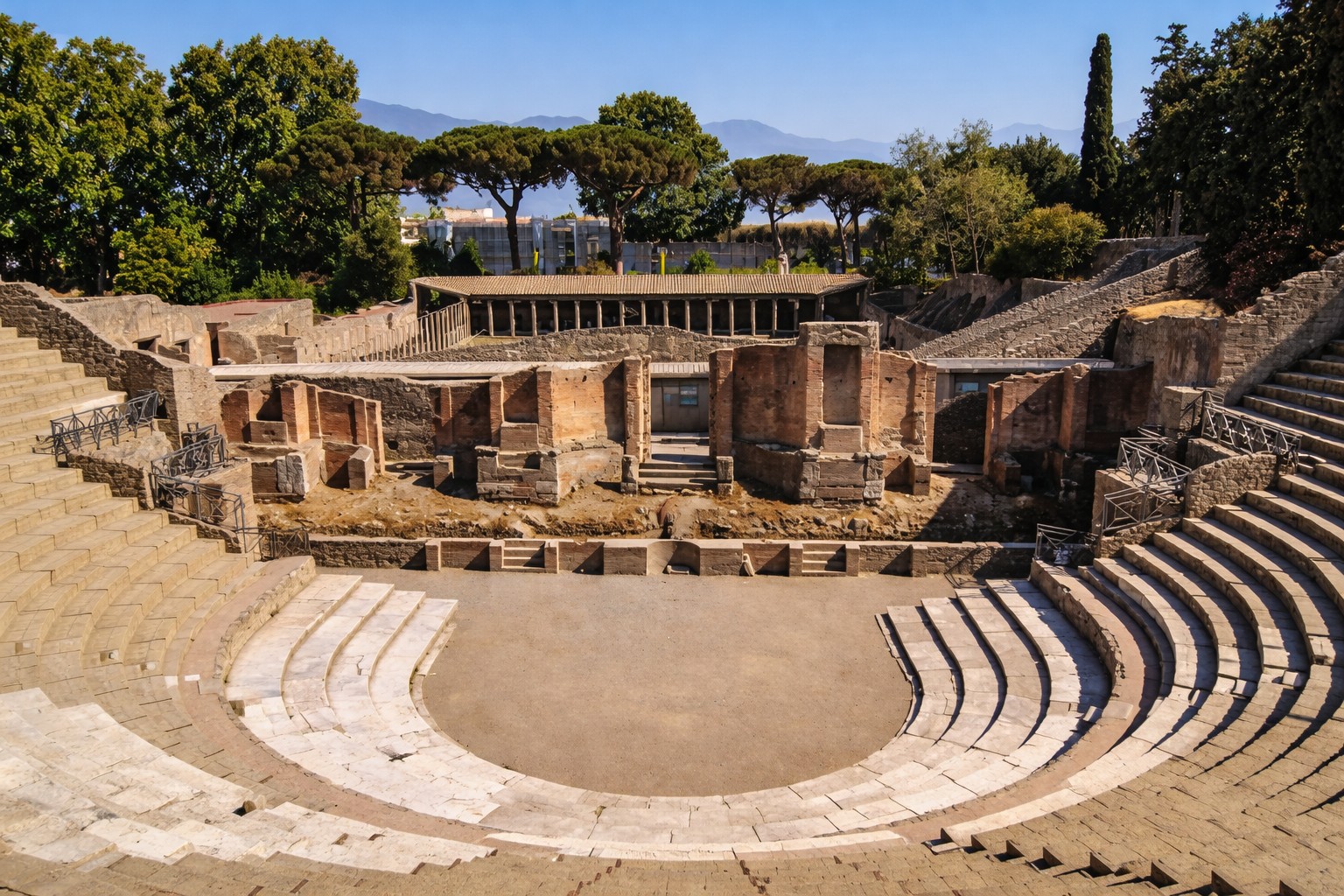 Teatro Grande von Pompei mit halbrundem Zuschauerraum, steinernen Sitzreihen und Blick auf die erhaltenen Bühnenreste, eingerahmt von Bäumen und Hügeln im Hintergrund